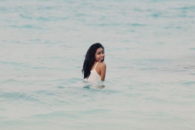 Portrait of smiling young woman standing in sea