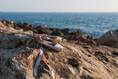 Close-up of abandoned ballet shoes on rock formation with sea in background