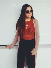 Portrait of young woman wearing sunglasses standing against wall