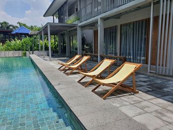 Empty chairs by swimming pool against house