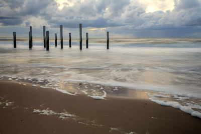Wooden posts on beach against sky