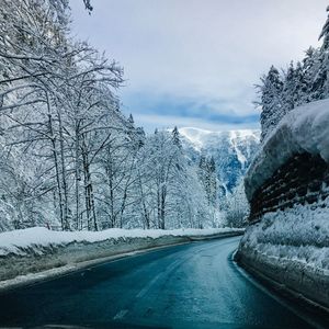 Snow covered road by trees against sky