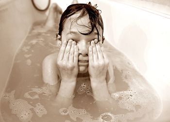 Boy eyes covering with hands while sitting in bathtub