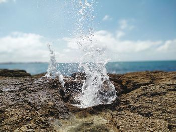 Waves splashing on rocks at shore against sky