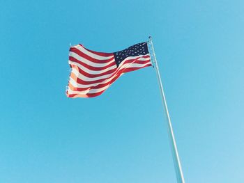 Low angle view of american flag waving against clear blue sky