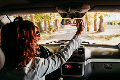 Rear view of woman adjusting rear-view mirror in camper trailer