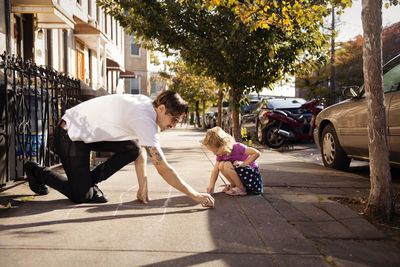 Father and daughter drawing hopscotch on footpath