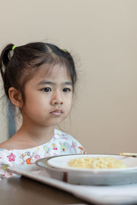 Thoughtful girl with food on table sitting against wall at home