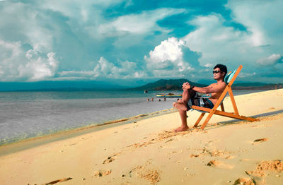 Full length of men sitting on beach against sky
