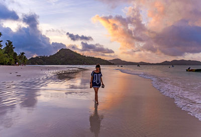 Rear view of woman standing on beach against sky during sunset