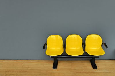 Deserted yellow seats on gray wall at waiting room woodden floor