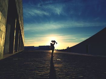 Mother carrying daughter while standing on road against sky during sunset