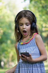 Smiling girl listening music while standing at park