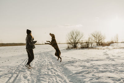Teenage girl playing with dog in snow at winter sunrise
