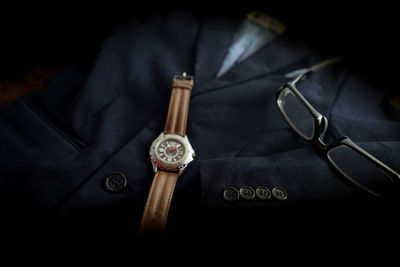 Close-up of wristwatch by eyeglasses on blazer