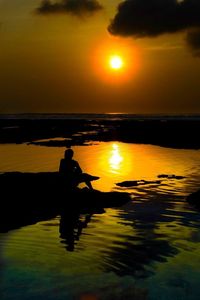 Silhouette man by sea against sky during sunset