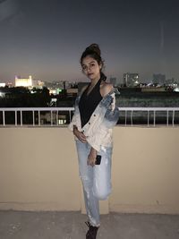 Portrait of young woman standing against cityscape at night