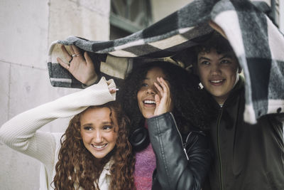 Smiling boy covering teenage female friends with flannel shirt during rain