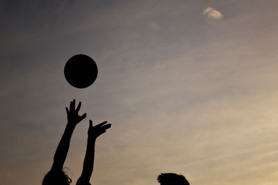 Cropped image of friends playing basketball against sky during sunset