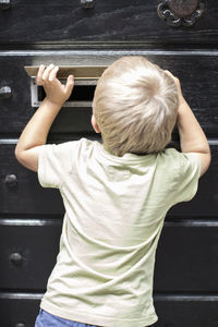 Rear view of little boy looking through mail slot of door