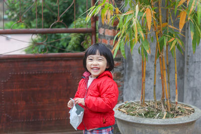 A vietnamese young little kid is laughing with a cake bag in a hand near a bamboo tree