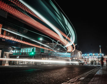 Light trails on bridge over city against sky at night