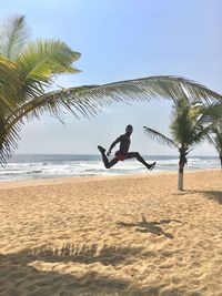 Portrait of man jumping at beach against sky