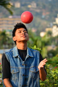 Close-up of young man playing with ball while standing against plants