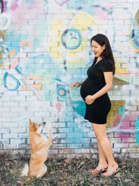 Full length portrait of young woman sitting on wall