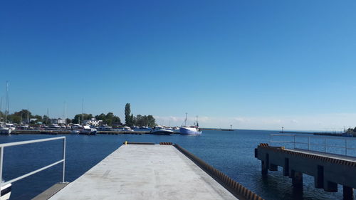 Sailboats on pier by sea against clear blue sky
