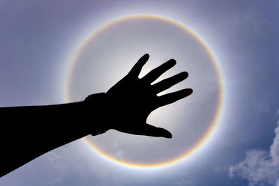 Silhouette hand against rainbow in sky