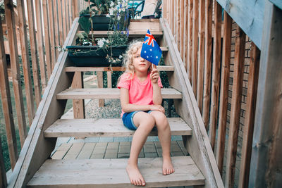 Caucasian girl holding australian flag. child sitting on backyard at home holding australia flag. 