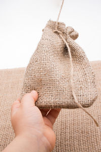 Close-up of hand holding jute pouch against white background