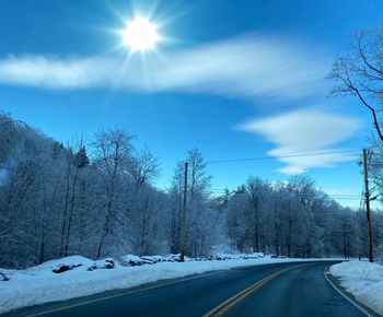 Snow covered road amidst trees against sky