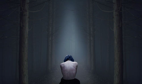 Rear view of shirtless woman sitting in forest