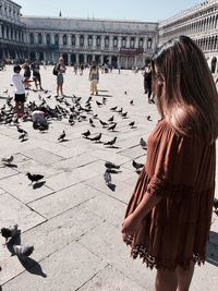 Side view of woman standing by pigeons at piazza san marco