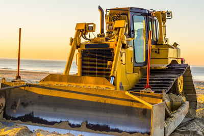 Construction site by sea against sky during sunset