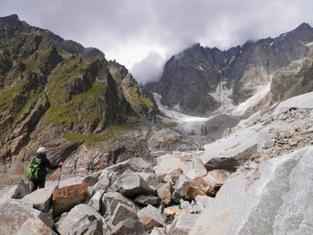 Rear view of person hiking on rocky mountains against cloudy sky