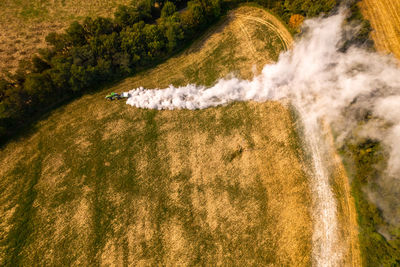 Aerial view of a tractor spreading lime on fields to improve soil quality after the harvest. 