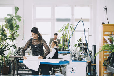 Female entrepreneur ironing white fabric while colleagues working in background at creative office