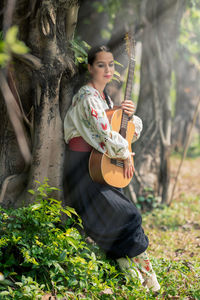 Young woman standing by tree trunk