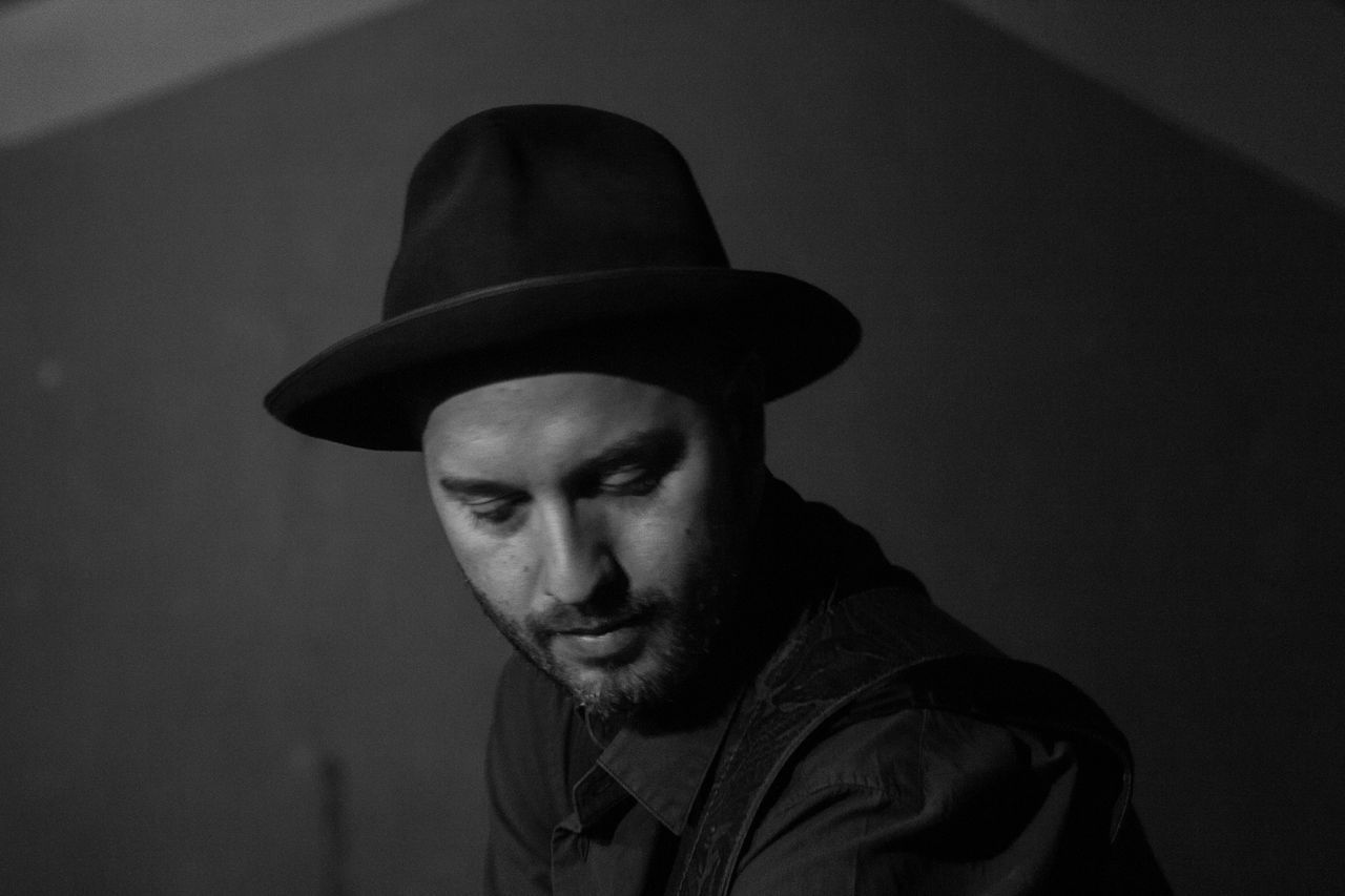 Young man wearing hat looking down while sitting against wall