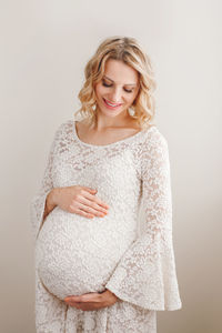 Smiling pregnant woman touching abdomen against white background