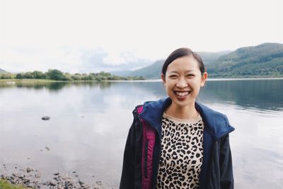 Portrait of smiling young woman standing by lake against sky