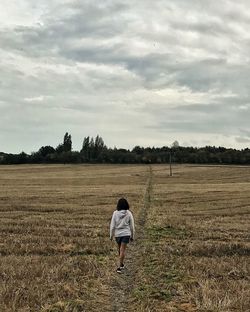 Rear view of man walking on field against sky