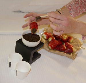 Cropped hands of woman applying chocolate sauce on strawberry