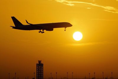 Silhouette airplane flying against sky during sunset