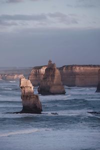 Rock formations in sea against sky at dusk 