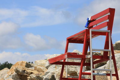 Red metallic lifeguard chair structure against sky