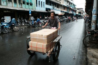 Close-up of mature man with boxes over push cart on road in city